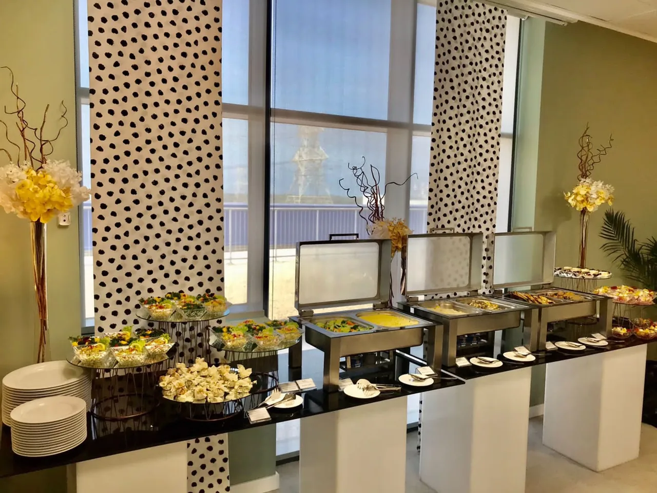 Buffet table with chafing dishes, plates and a floral arrangement.