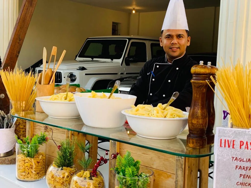 Chef at a live pasta station with pasta varieties and sauces.