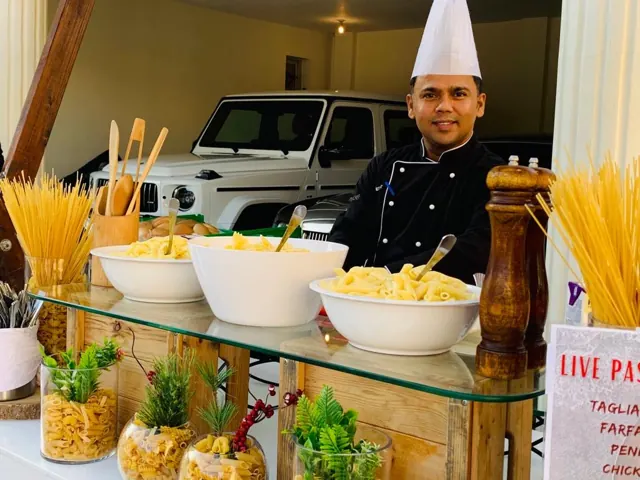 Chef at a live pasta station with pasta varieties and sauces.