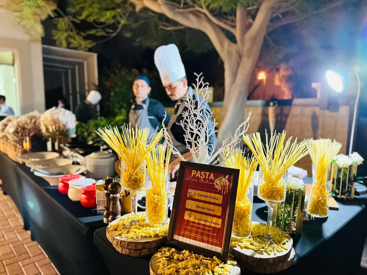 Chef at an evening pasta station in a garden.