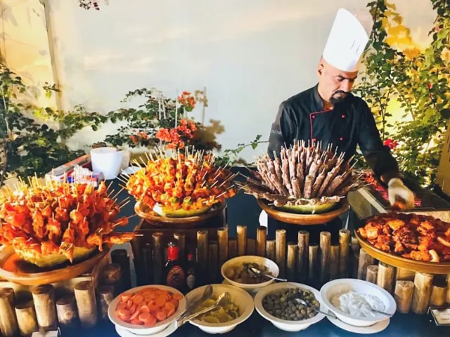 Chef behind a warmly lit BBQ buffet with skewers and sauces.