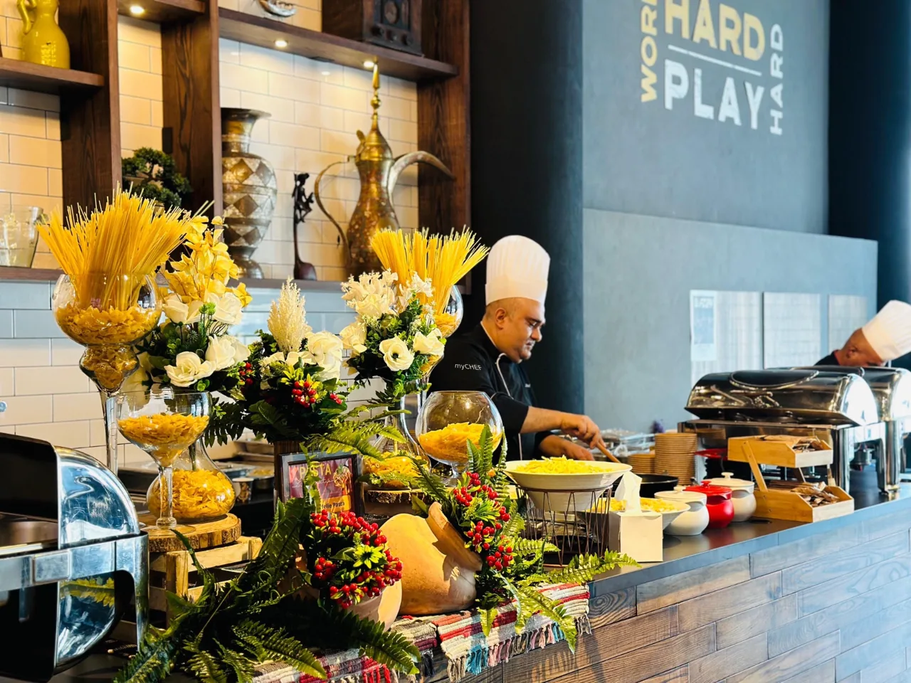 Chef behind an indoor pasta station with ingredients and serving bowls.