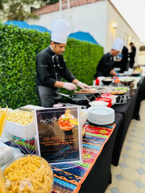 Chef preparing pasta at an outdoor live cooking station.