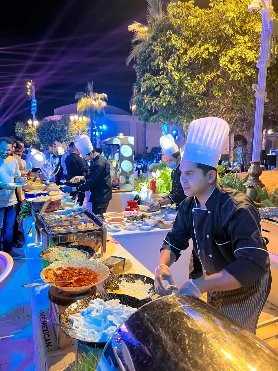 Chef serving from a live cooking station at an evening event.