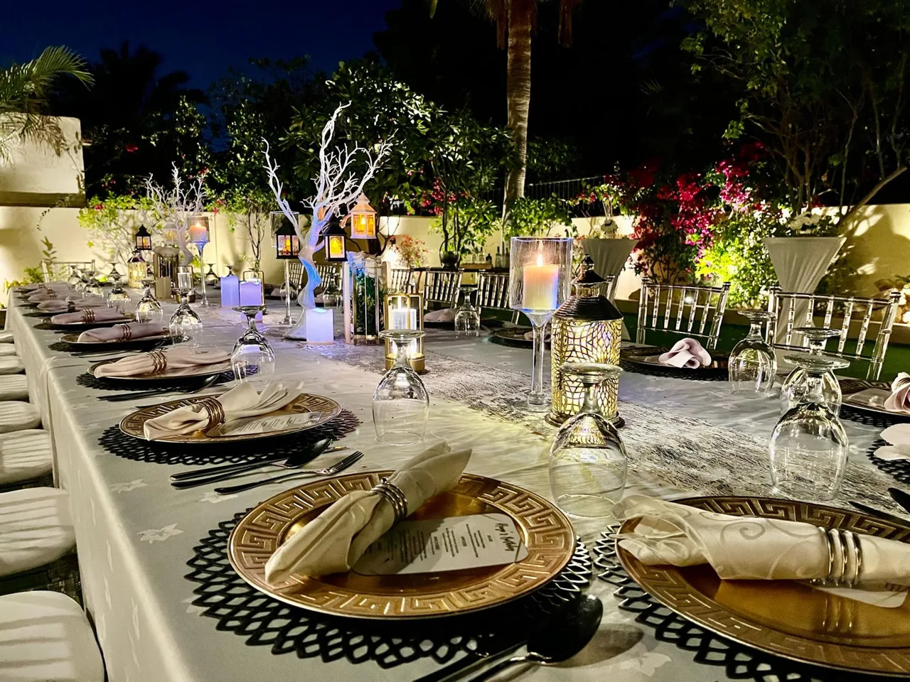 Garden dining table with candles, glassware and greenery at night.