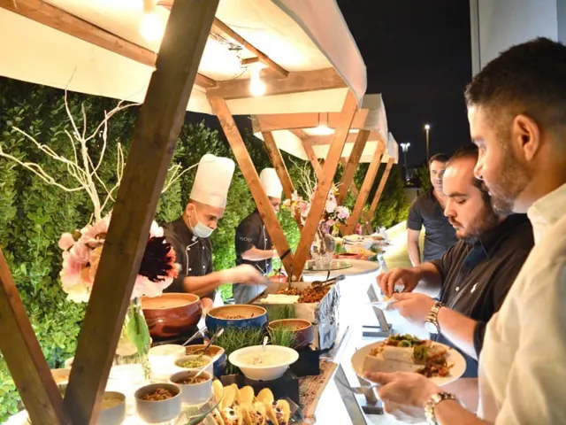 Guests being served at live cooking counters beneath an outdoor structure.