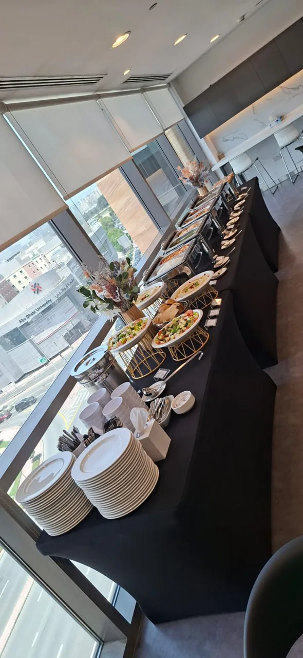 Indoor buffet with food displays beside large windows.