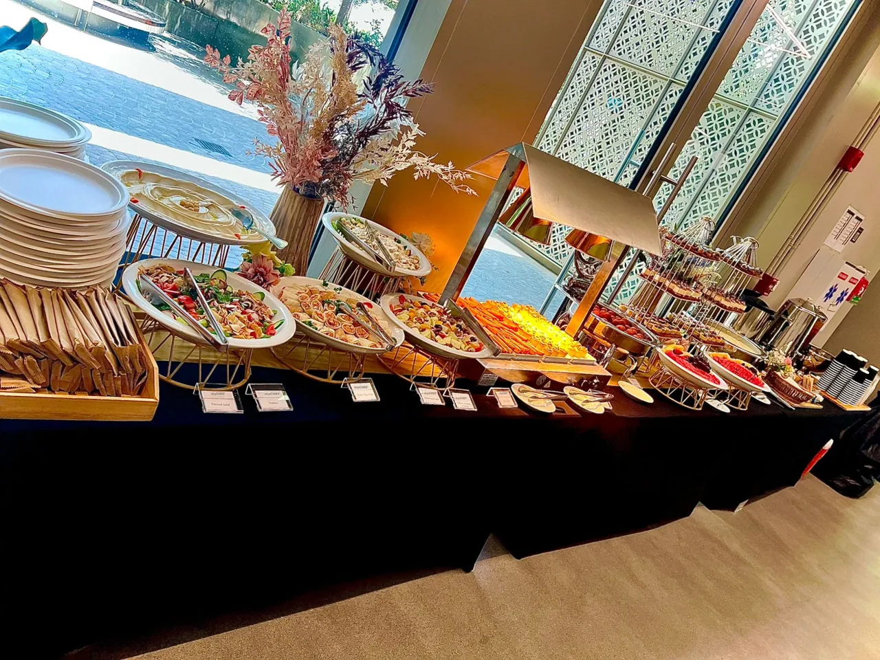 Indoor buffet with salads, bread, warm dishes and stacked plates.