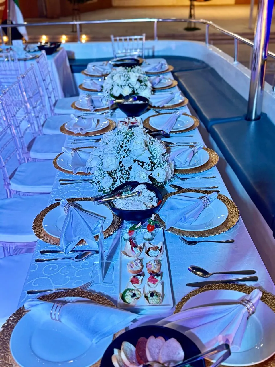 Long dining table set on a yacht deck with coloured lighting.