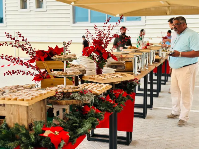 Long festive buffet with wooden serving stands and red flowers.