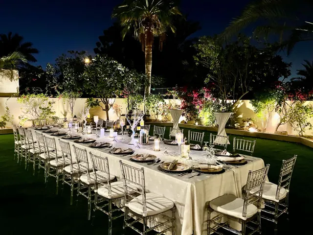 Long garden dinner table set with white chairs at night.