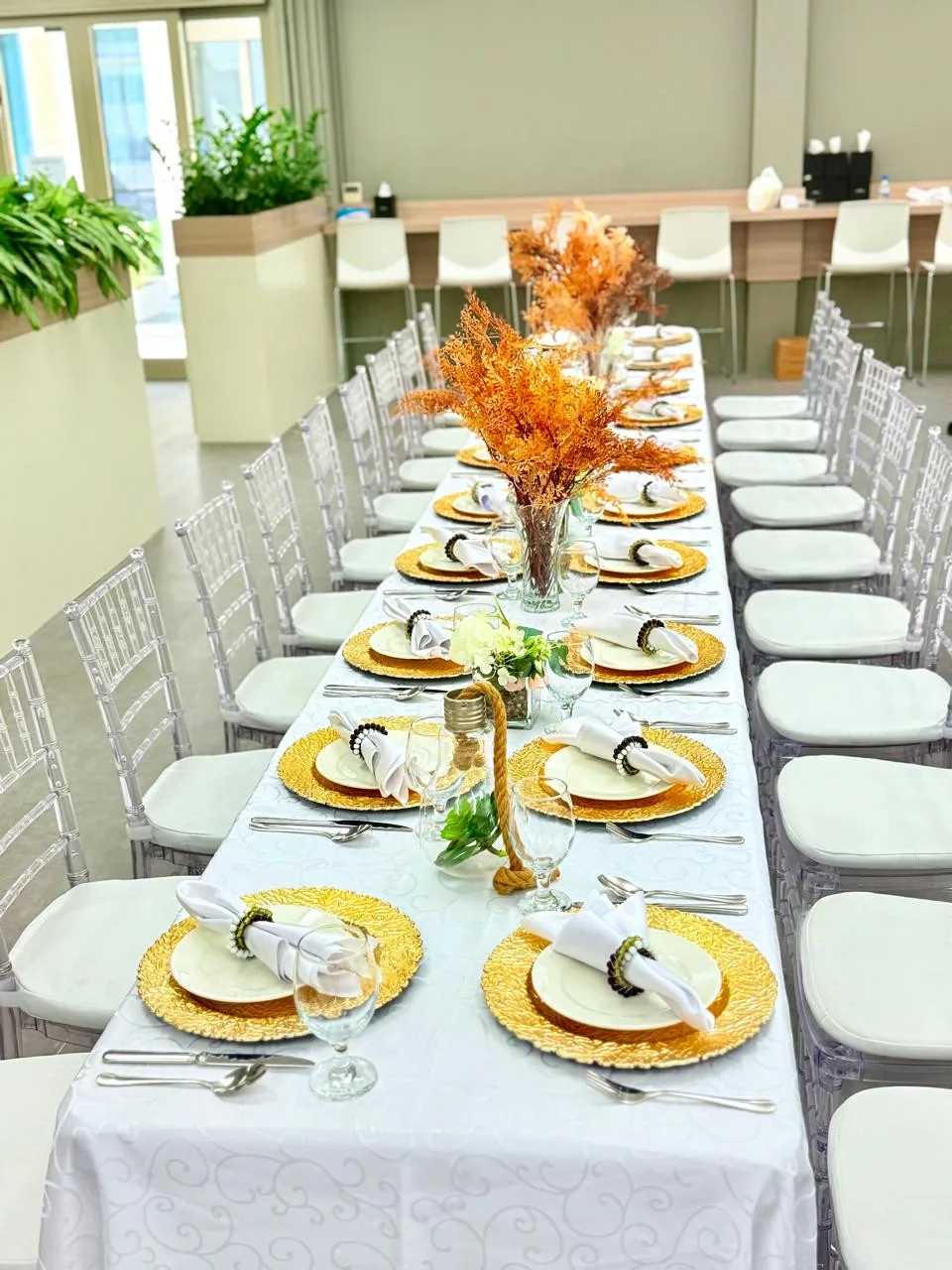 Long indoor dining table set with plates, glasses and chairs.
