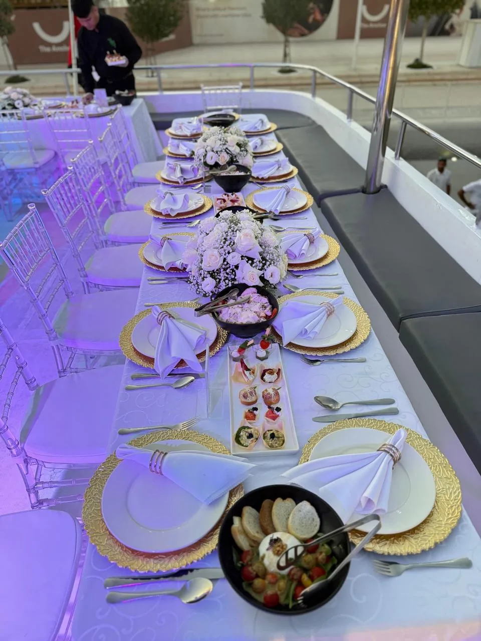 Long yacht dining table with gold chargers, flowers and glassware.