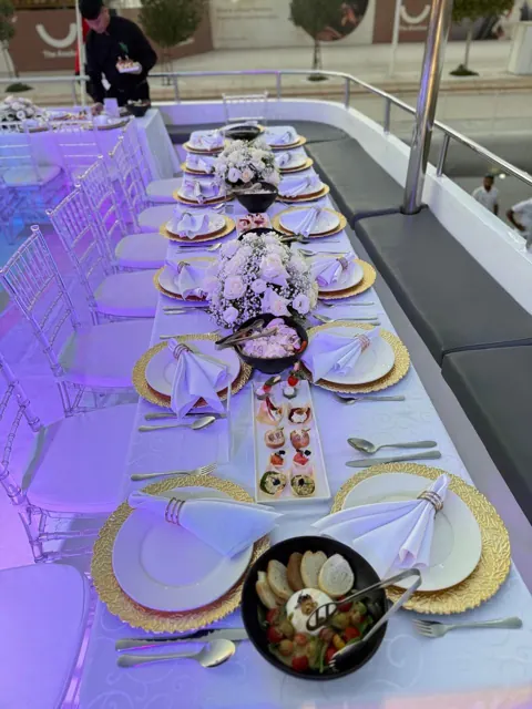 Long yacht dining table with gold chargers, flowers and glassware.