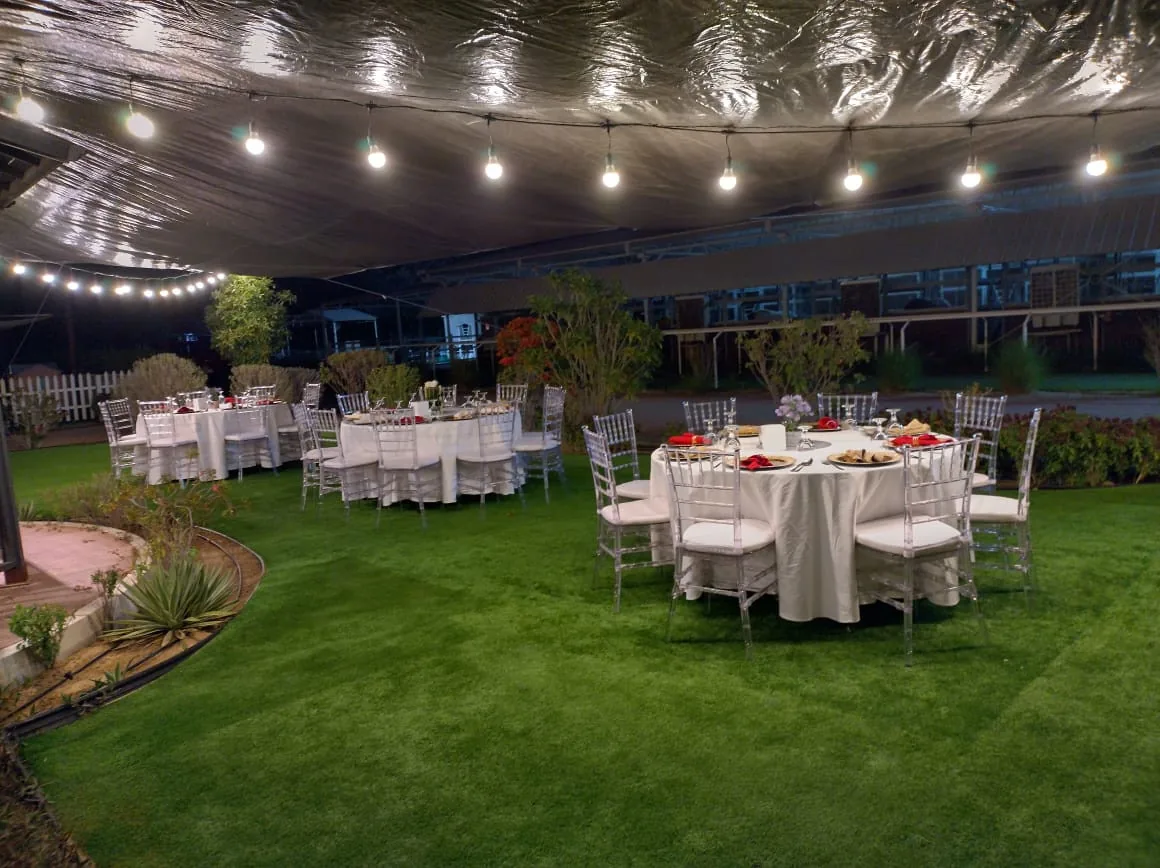 Round dinner tables set in a garden beneath string lights.