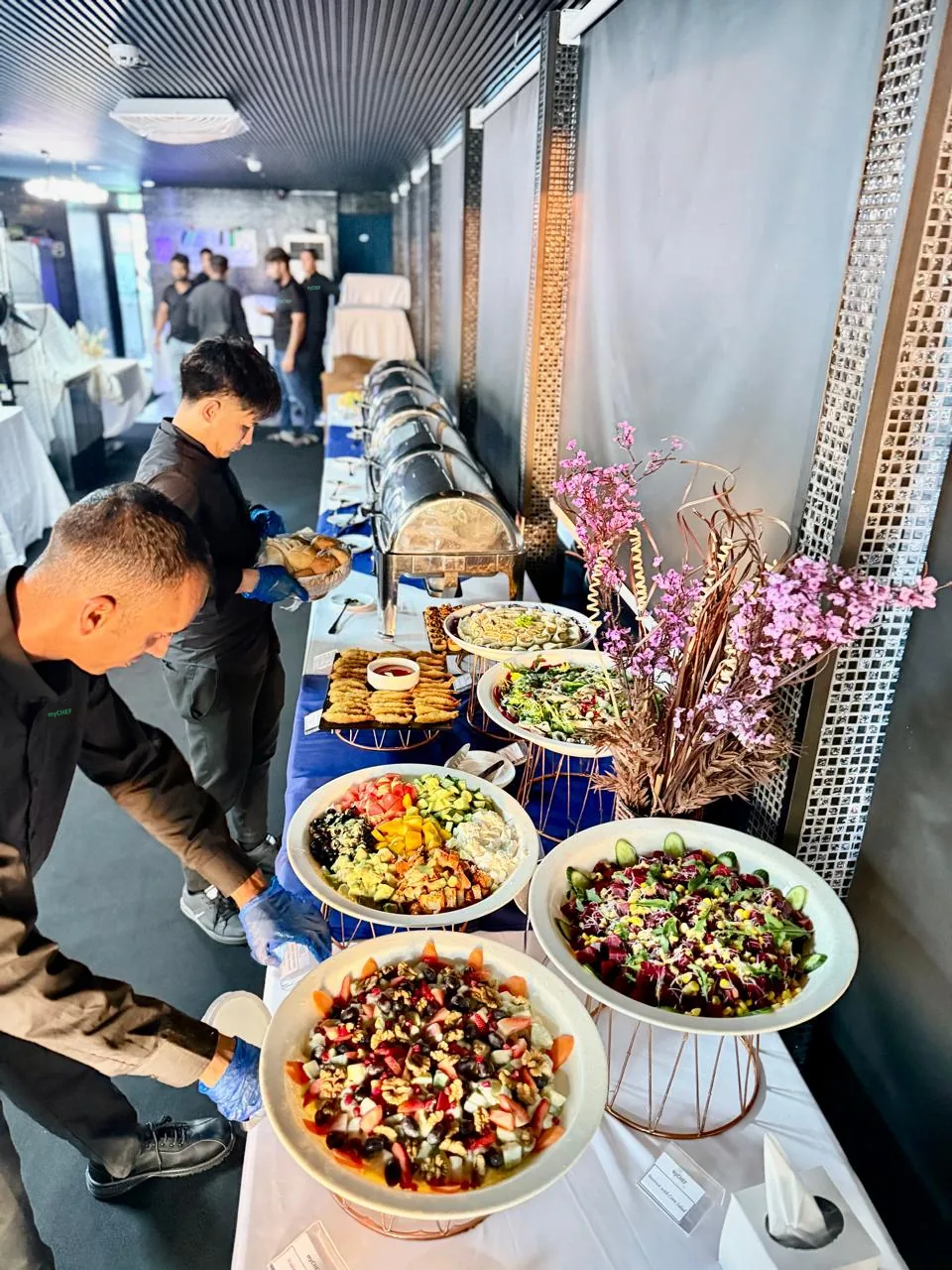 Service team arranging food at a long indoor buffet.