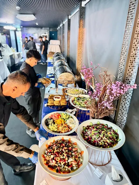 Service team arranging food at a long indoor buffet.