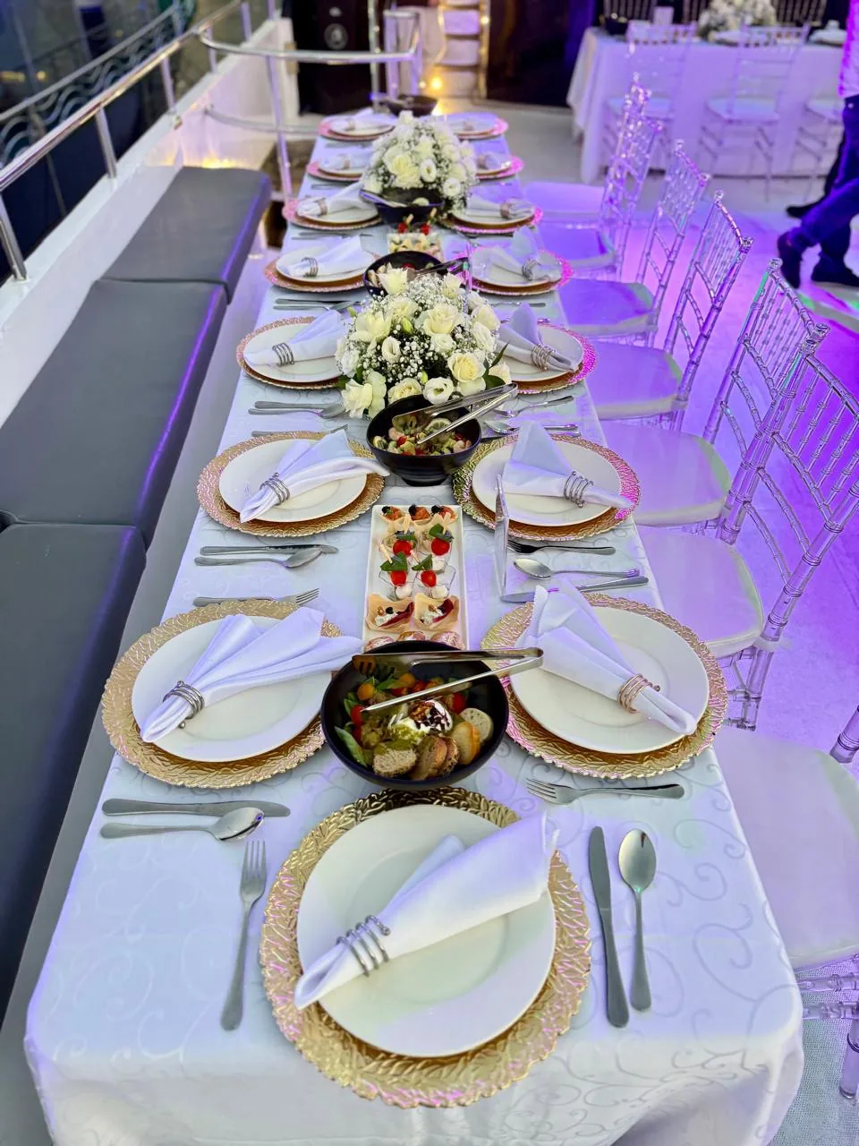 Yacht deck table set with white chairs and floral centrepieces.